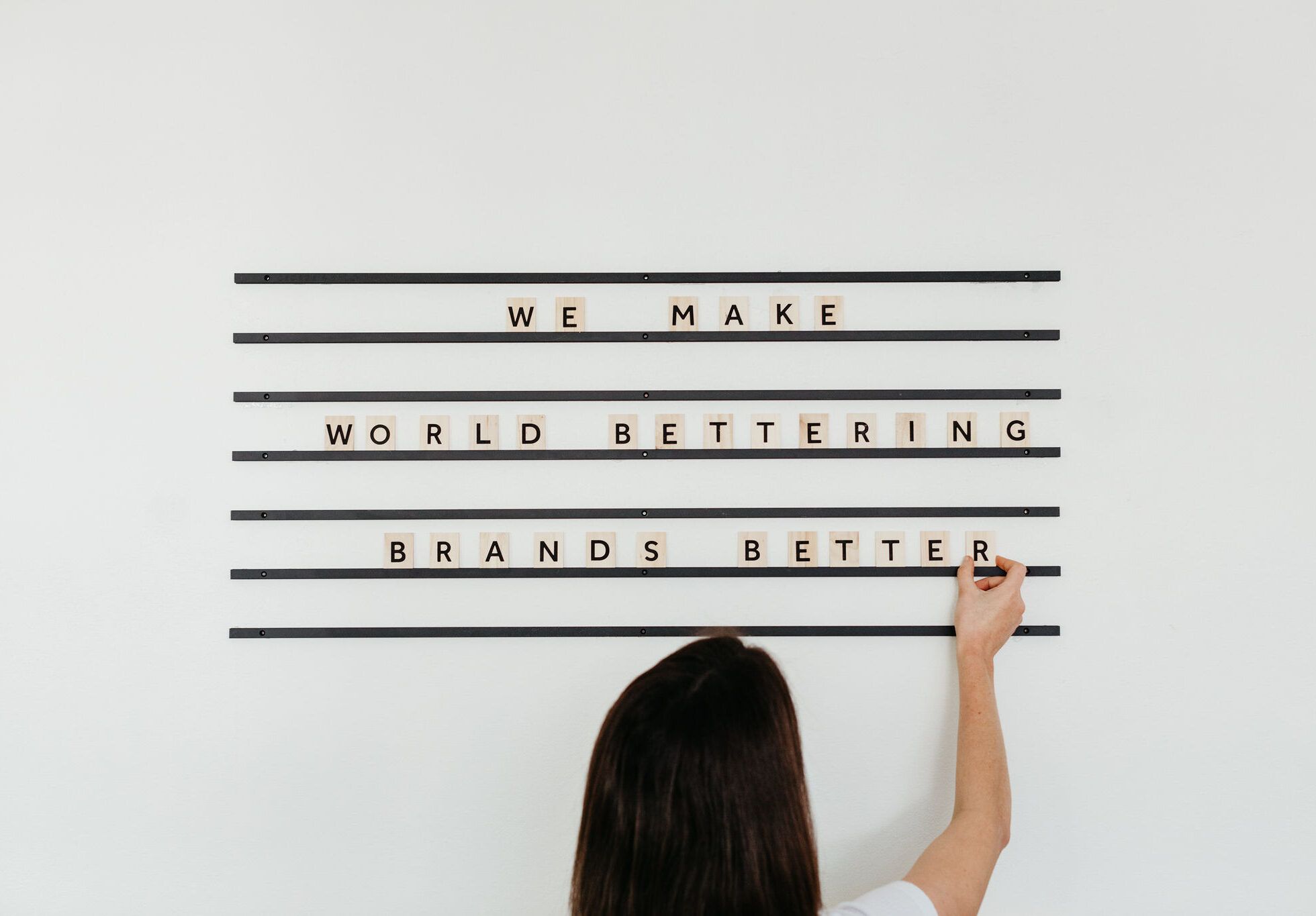 Person adds tiles to a sign on the wall which reads 'We make world bettering brands better'